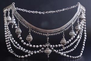 Intricate silver jewelry with hanging ornaments displayed against a dark background photo