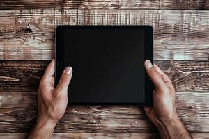 Person holding a blank tablet over a wooden table in a cozy indoor setting photo
