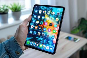 A person holds a tablet displaying a vibrant home screen with apps in a bright room filled with plants photo