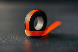 Close-up of a roll of black and orange tape on a textured surface in a well-lit environment photo
