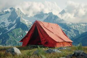 Bright red tent pitched in grassy field with mountains and clouds in the background during daylight photo