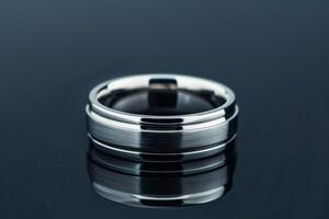 A close-up view of a silver wedding band placed on a reflective surface photo