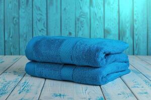 Soft blue towels stacked neatly on a rustic wooden surface with a turquoise backdrop photo