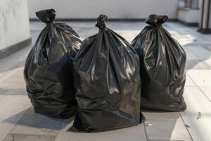 Three black trash bags placed on a tiled floor in a clean outdoor setting during daylight photo
