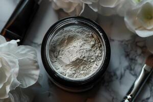 Powder in a jar surrounded by flowers and cosmetic tools on a marble surface photo