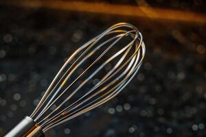 Close-up of a stainless steel whisk against a dark background with soft light reflections photo