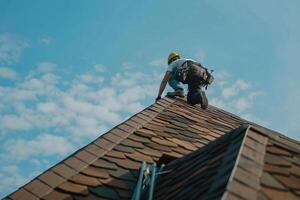 Worker repairs a sloped roof under a clear blue sky during daylight hours photo