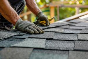 Worker installing shingles on a residential roof during daylight hours in a suburban area photo