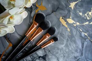 Elegant makeup brushes arranged on a stylish marble surface with gold accents and white orchids photo