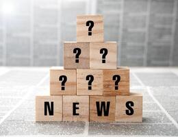 News title and question marks on square wooden blocks on a newspaper background photo