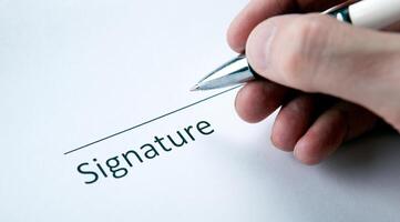 One document with a place for a signature and a hand of a man with a pen photo
