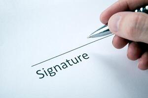 One document with a place for a signature and a hand of a man with a pen photo