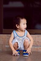 Asian little boy aged 1-2 years old squatting on the floor, the child with dirty face after from playing with magic color pen is sitting and looking at something. In evening. Positive mood. Vertical. photo