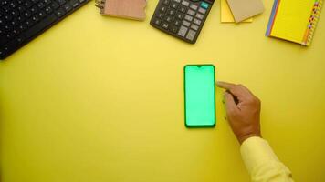 Top view of a person's hand holding a green smartphone on a yellow background video
