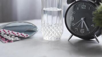 A glass of water, pills and an alarm clock video