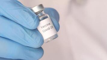 A person in blue gloves holding a vial with a label that says vaccine video