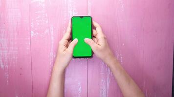 A woman's hand holding a smartphone with a green screen on a pink background video