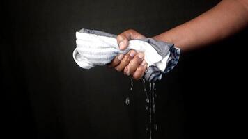 slow motion of Hands squeeze wet towel against black background. draining water from wet towel.. video