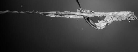 Stirring drinks by bar spoon. Underwater of silver metal bar spoon stir clear alcoholic drinks such as Vodka Gin or Tequila close up shot. Bartender spoon under clear water against grey background. photo