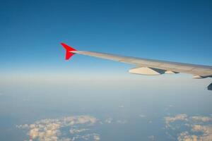 view of the blue clear sky from the height of flight above the clouds from the window of the plane in the bright sun. part of an airplane wing in the frame photo
