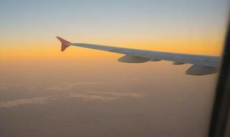 view of the sunset sky from the height of the flight above the clouds from the window of the aircraft. part of an airplane wing in the frame photo