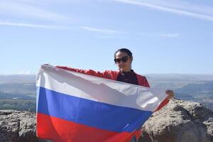 The Russian flag is on the shoulders of a girl standing against the backdrop of the Caucasus mountains. Unity Day in Russia. photo