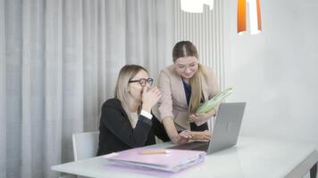 Two women laugh in front of the computer in the office video