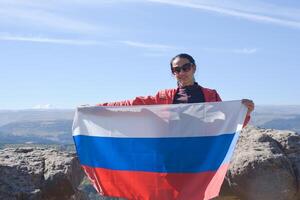 The Russian flag is on the shoulders of a girl standing against the backdrop of the Caucasus mountains. Unity Day in Russia. photo