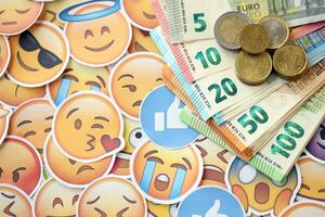KYIV, UKRAINE - APRIL 20, 2024 European euro money and large set of stickers with Emoji yellow faces. The concept of smm, smo paid service for boost in social media photo