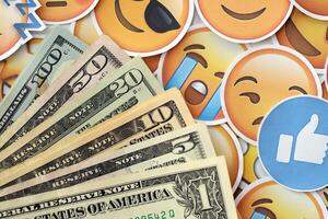 KYIV, UKRAINE - APRIL 20, 2024 USD dollars money and large set of stickers with Emoji yellow faces. The concept of smm, smo paid service for boost in social media photo