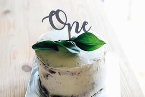 cake decorated with a sprig of greens and a wooden inscription one. cake for 1 year to the child photo