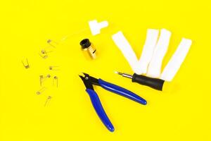 electronic cigarette details, Vata, coils, drip, spring, nippers on a yellow background. flat lay vape photo