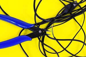 tangled charger wires. Black wire on a yellow background with blue nippers photo