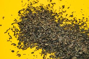 large leaf green tea scattered on a yellow background. close-up photo