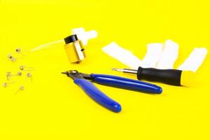 electronic cigarette details, Vata, coils, drip, spring, nippers on a yellow background. flat lay vape photo