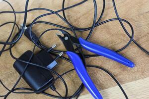 tangled charger wires. Black wire on a yellow background with blue nippers photo