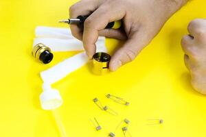 electronic cigarette details, Vata, coils, drip, spring, nippers on a yellow background. man's hands change springs in vape photo
