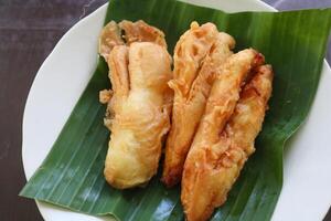 fried bananas or pisang goreng served on a plate with banana leaf. The plate is on a wooden table photo
