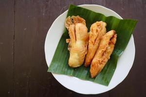 fried bananas or pisang goreng served on a plate with banana leaf. The plate is on a wooden table photo