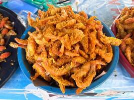 A bowl of fried shrimp is piled high on a table. The shrimp are golden brown and appear to be freshly cooked. traditional market photo
