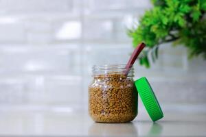 Fenugreek seeds in a plastic jar with green leaves on a white background photo