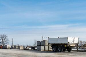 Construction site with empty car trailer and building materials stacked on pallets. photo