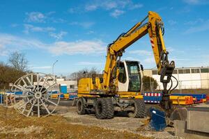 Yellow excavator at a construction site next to an empty cable drum. photo