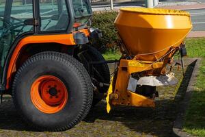 Orange rotating trailer on a tractor for spreading road salt on icy sections of the road. photo