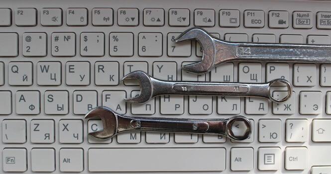 Engineering And Computer Hardware Concept. Three shiny mechanical wrenches laid out in order on computer keyboard top view photo