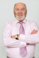 Portrait of an elderly gray-haired man with a beard and bald head. He has his arms crossed and is looking at the camera. photo