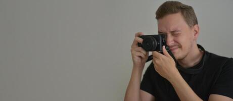 Young man with a photocamera. The photographer uses a camera to take a photo looking through lens. Professional photographing concept. Design banner background with copyspace for wallpaper or poster