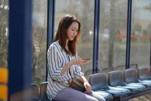 A girl sits alone at a bus stop using a mobile phone photo