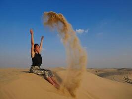A girl in the Dubai desert throws sand up and smiles photo