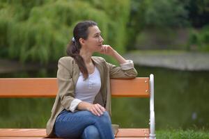 A woman sits on a park bench and looks thoughtfully to the right side photo